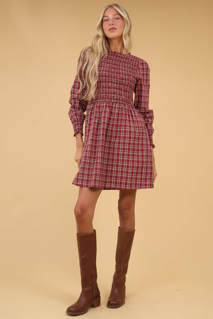 Young woman wearing a moest red plaid, short dress with long sleeves and smocked bodice.