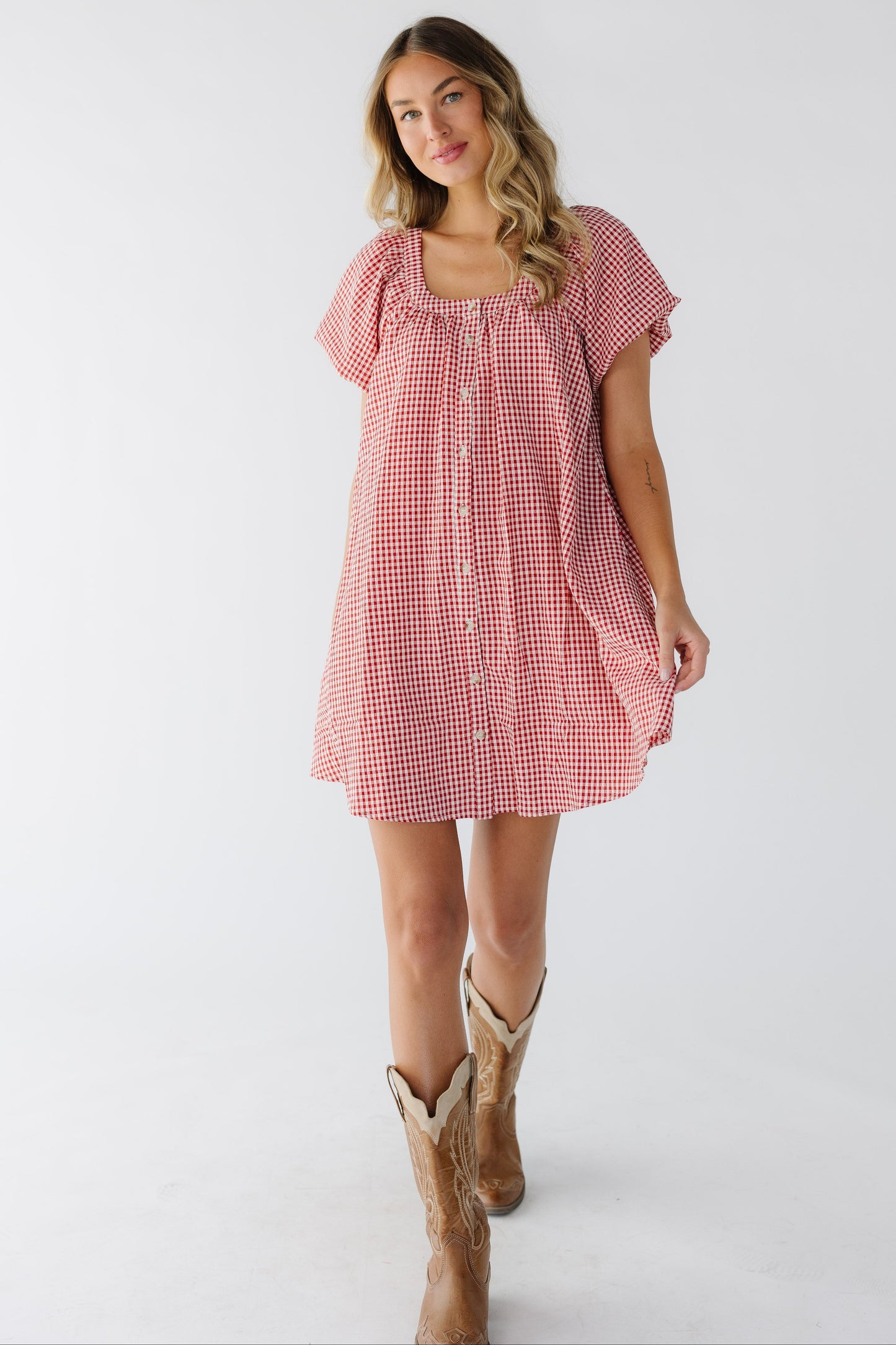 Young woman wearing a red & white button down gingham short dress with a scoop neckline and short balloon sleeves.