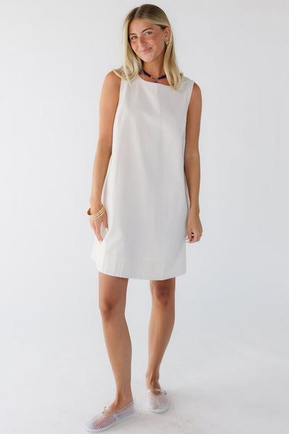 Woman wearing a cream sleeveless shift dress.