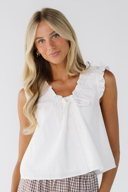 Woman wearing a loose fitting white blouse with ruffled arm openings and a ruffled scooped neckline.