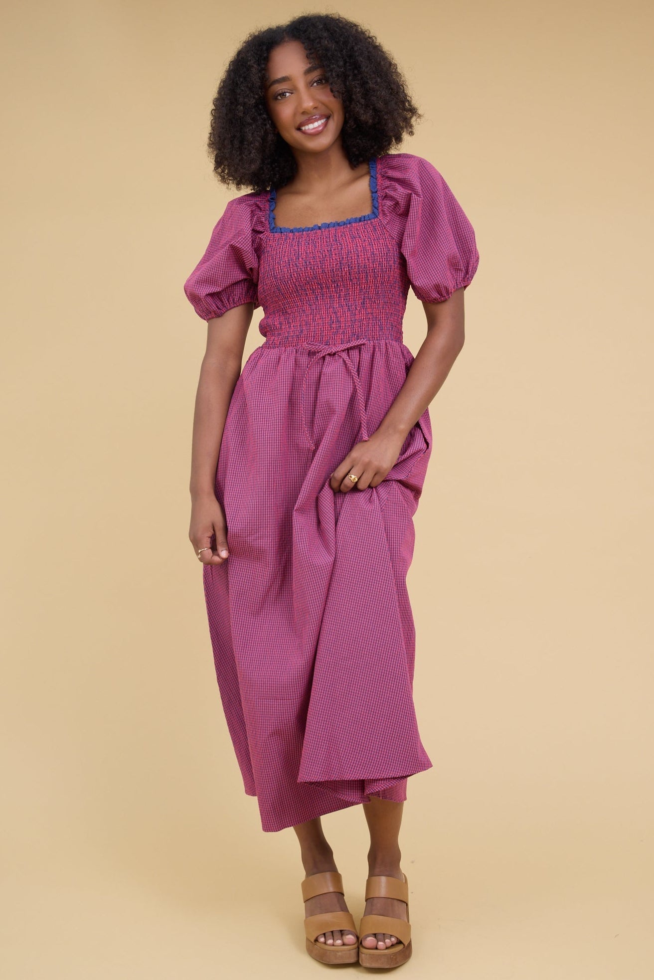 Woman wearing a red & blue gingham midi dress with a full skirt, smocked cbodice and balloon sleeves.
