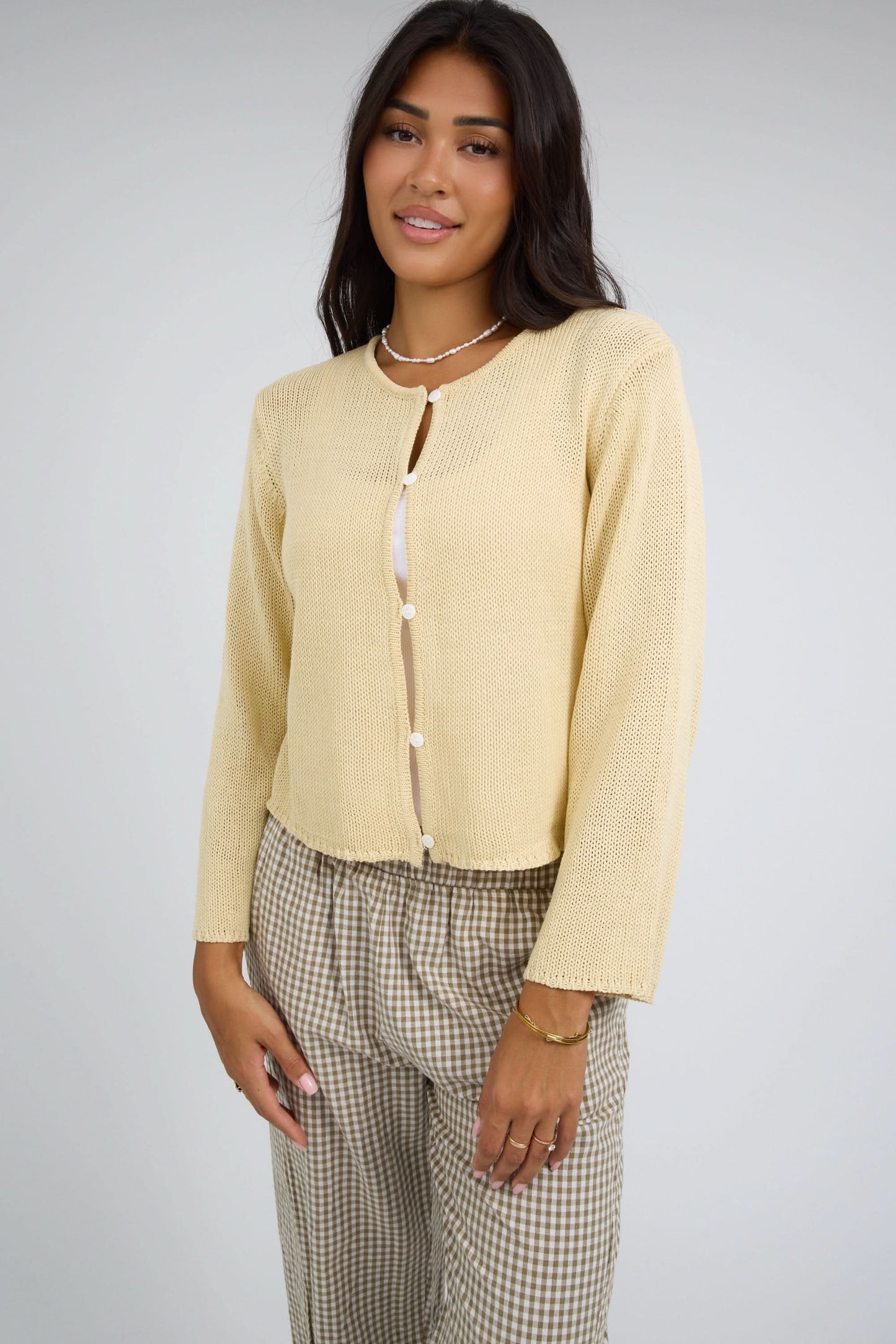 Woman wearing a loosely knit button down cardigan with a round neckline and long sleeves.