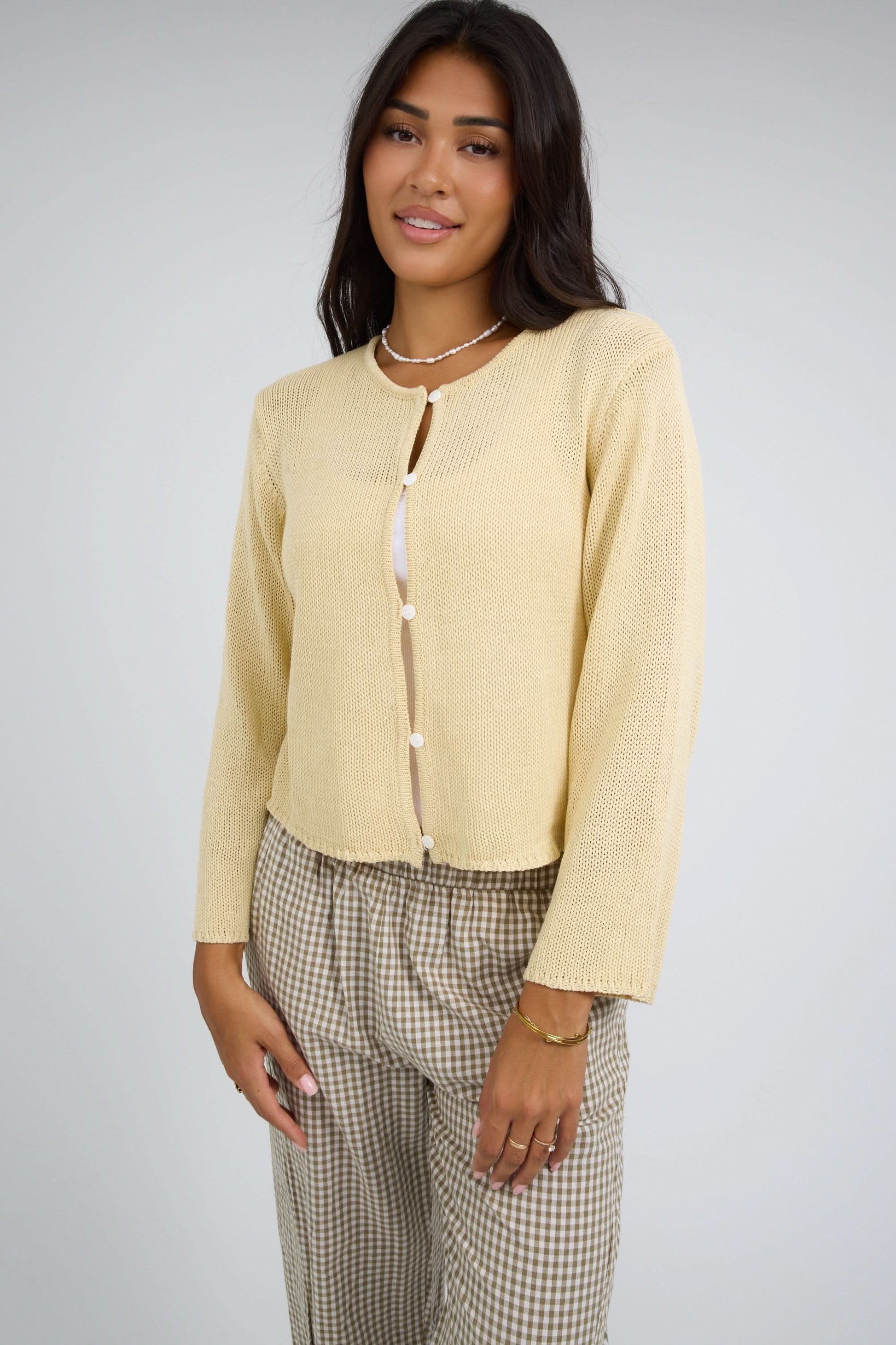 Woman wearing a loosely knit button down cardigan with a round neckline and long sleeves.