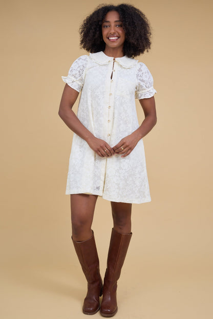 Woman wearing an all lace button down dress in off white with a lace collarand puff sleeves.