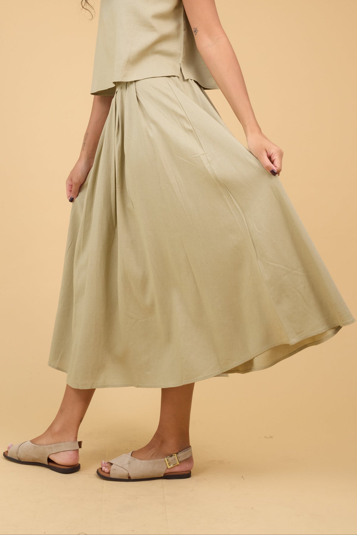Young woman wearing a light olive, pleated midi skirt.
