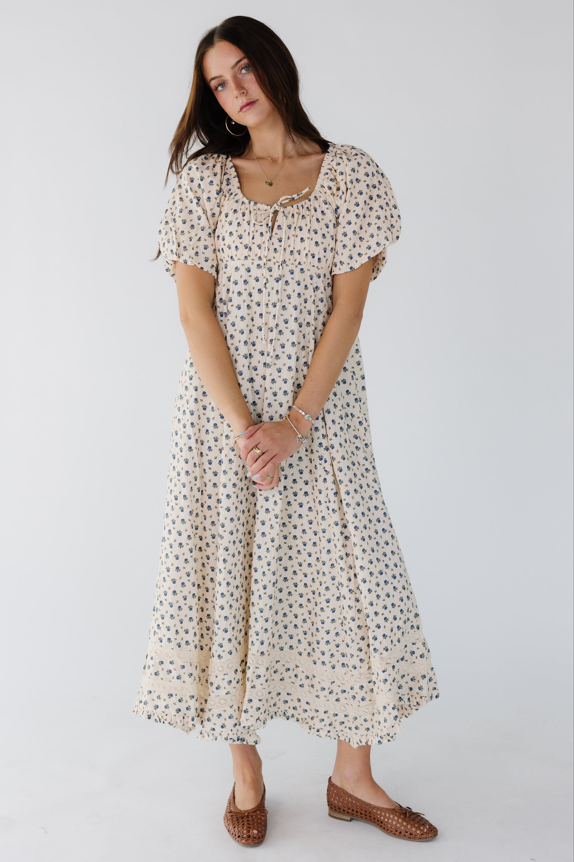 Woman wearing a cream & blue floral midi-maxi dress with a kercheif ruffle hem, lace insets and balloon sleeves.
