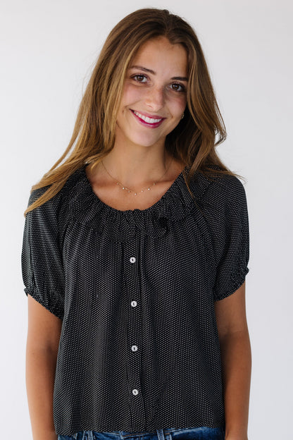 Woman wearing a modest black and white polka dot top that buttons down the front with short puff sleeves and a round neckline with a ruffle.