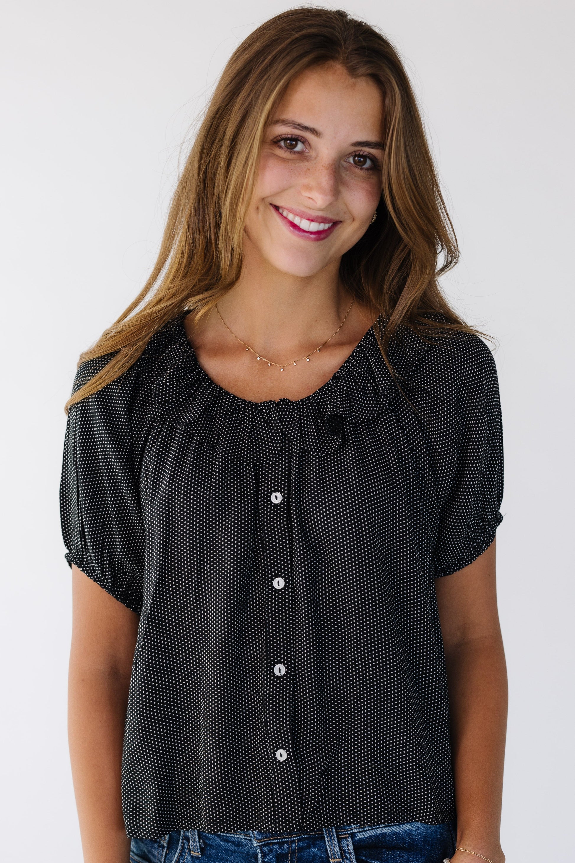 Young woman wearing a modest  black polka dot button down blouse with a round ruffled neckline and puff sleeves.