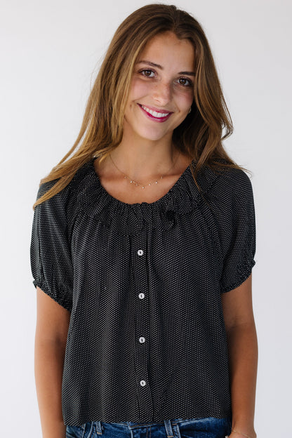 Young woman wearing a modest  black polka dot button down blouse with a round ruffled neckline and puff sleeves.