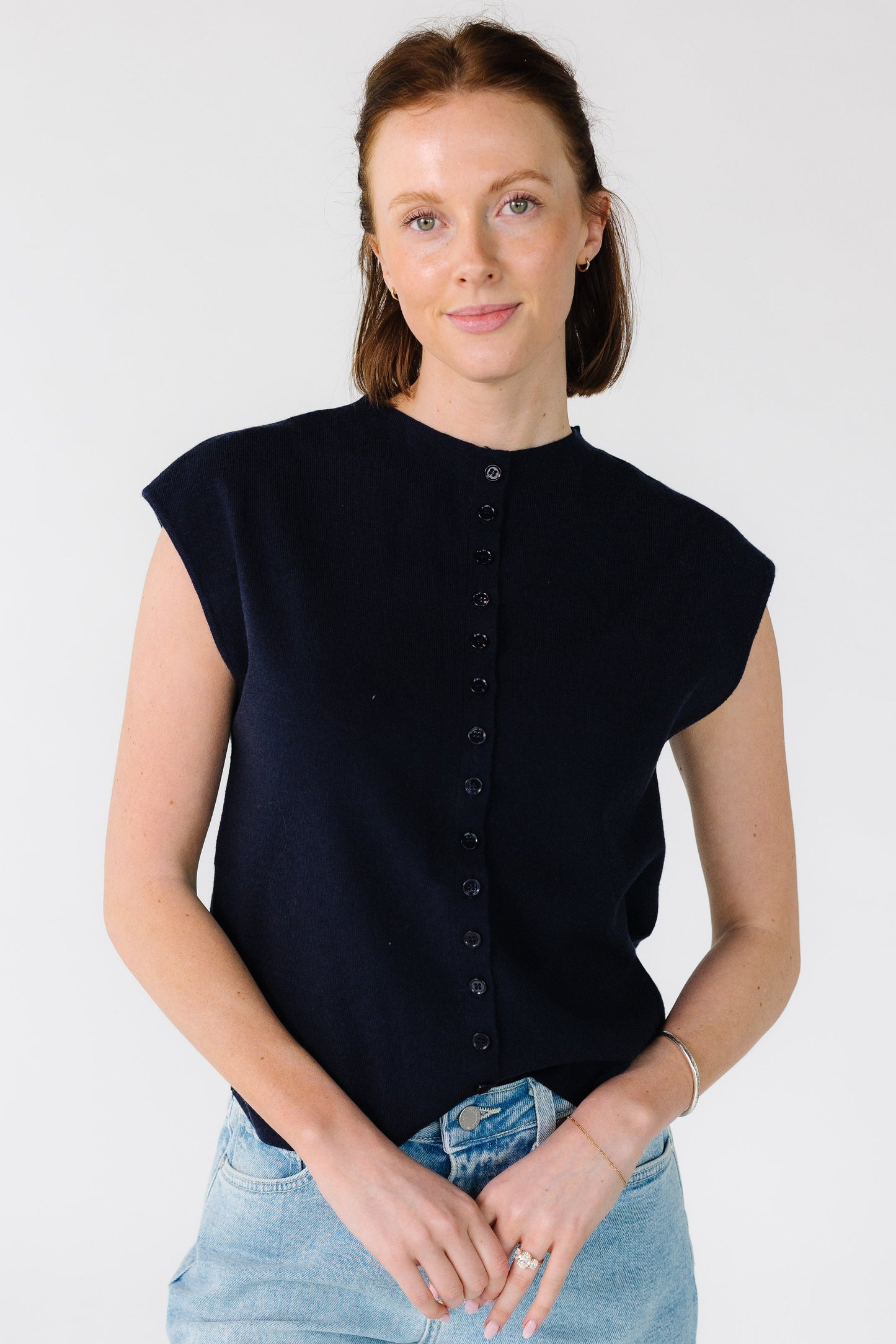 Young woman wearing a modest navy button down cardigan with a high round neckline and sleeveless.
