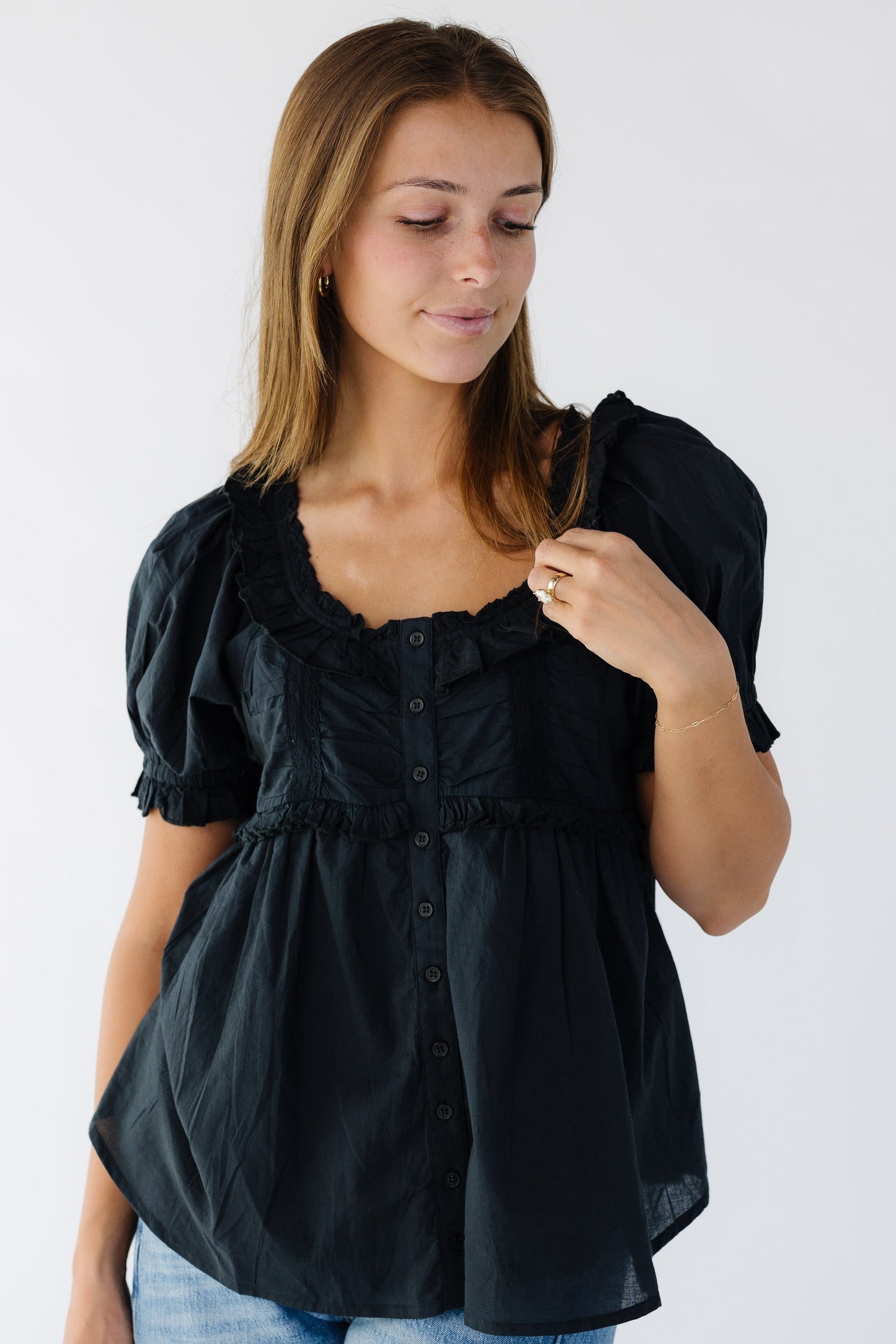 Young woman wearing a modest black flowy button down blouse with a scoop ruffled neckline and short puff sleeves.
