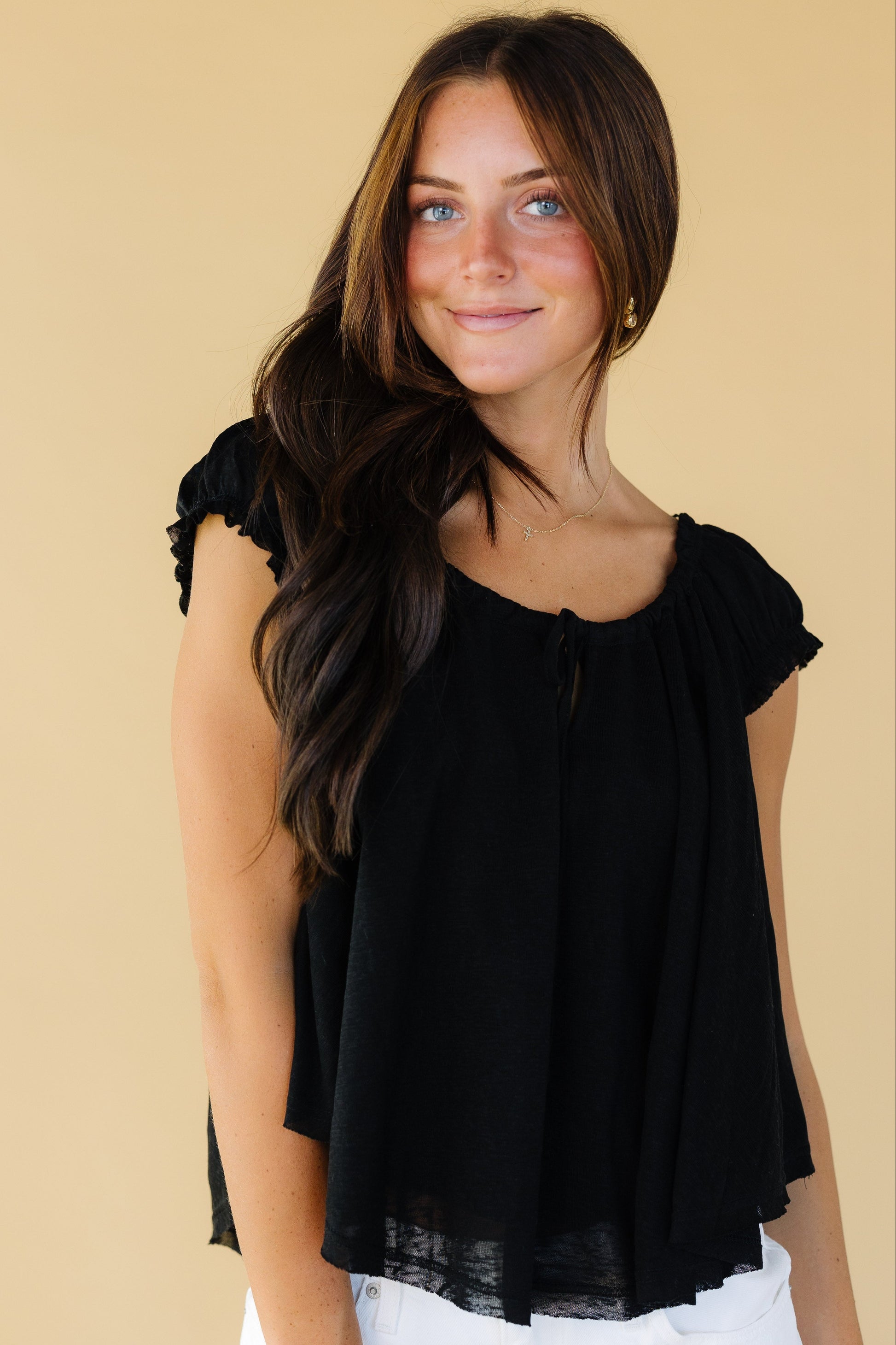 Young woman wearing a black flowy blouse with short cap sleeves and a scoop neckline.