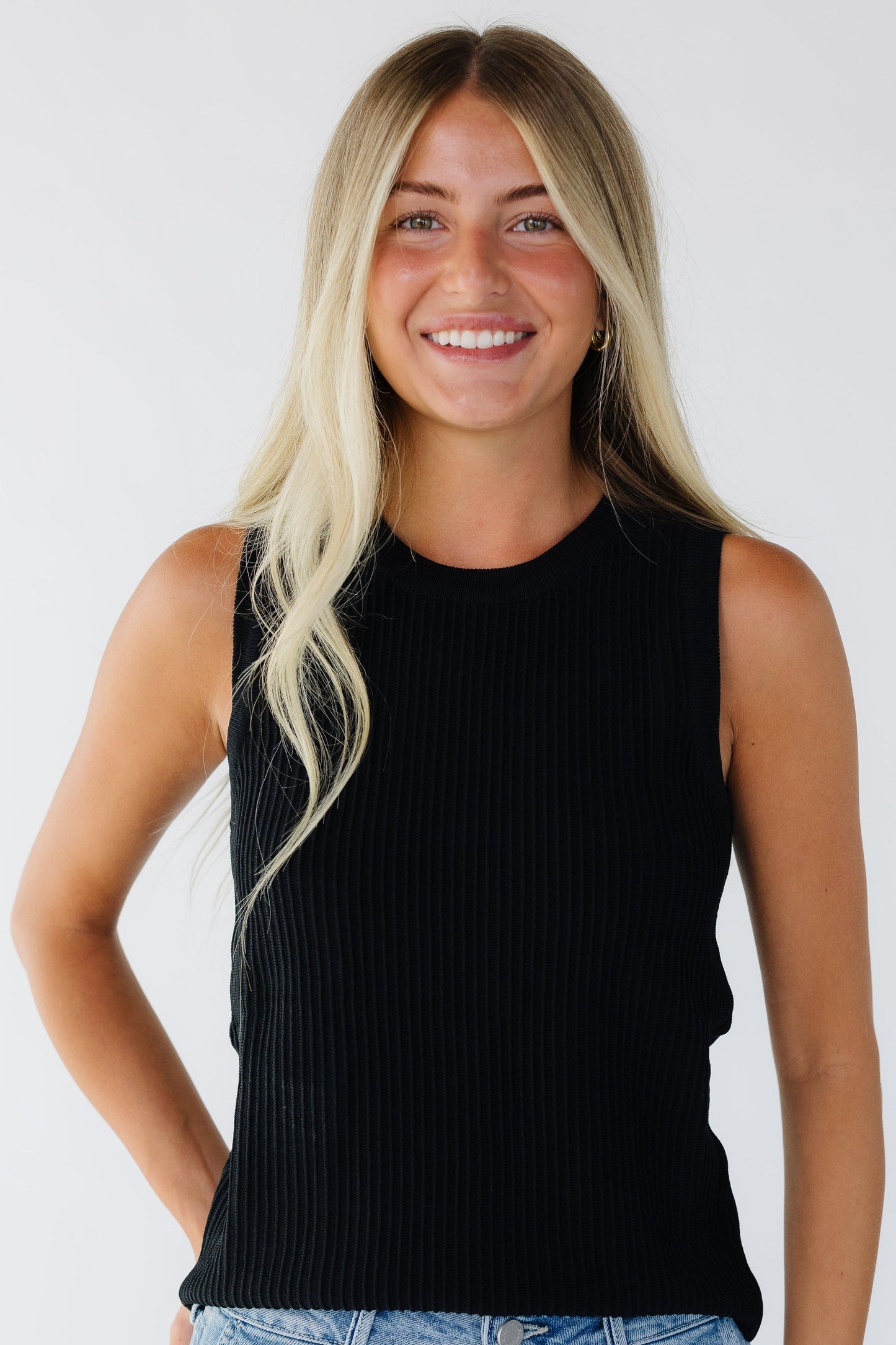 Woman wearing a black closer fitting tank top with a round neckline and a ridge stripe texture.