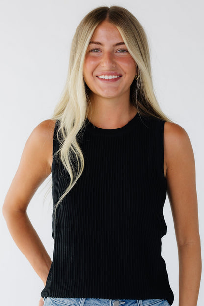 Woman wearing a black closer fitting tank top with a round neckline and a ridge stripe texture.