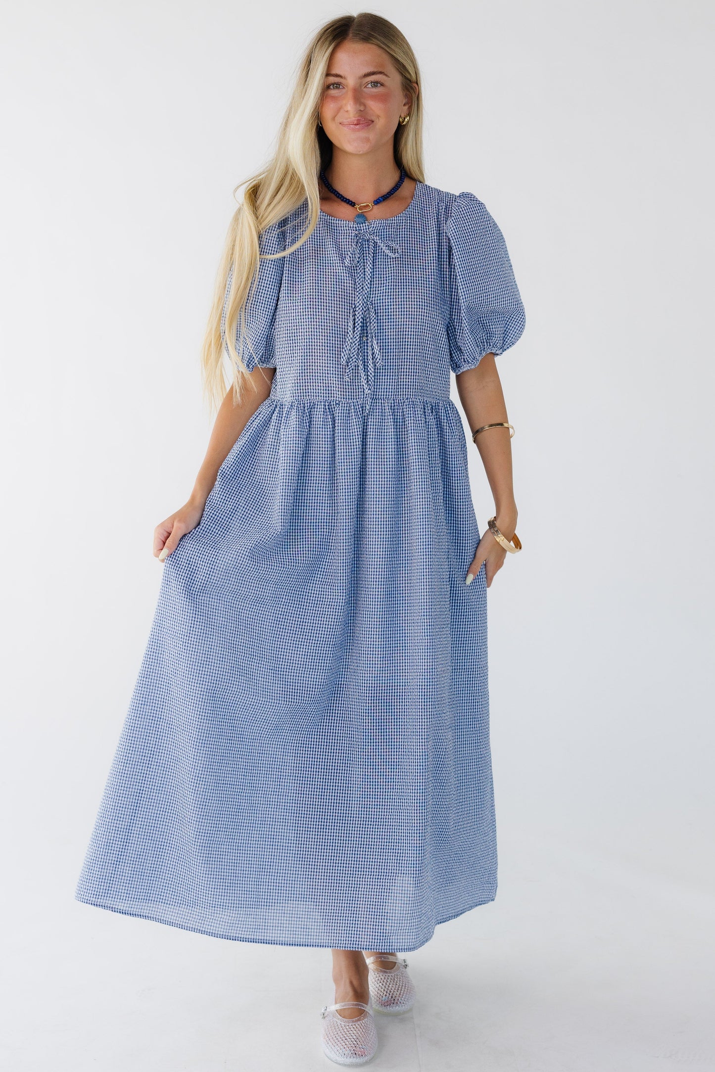 Woman wearing a loose fitting blue & white gingham midi dress with a loose fitting waist, wide bodice and balloon sleeves.