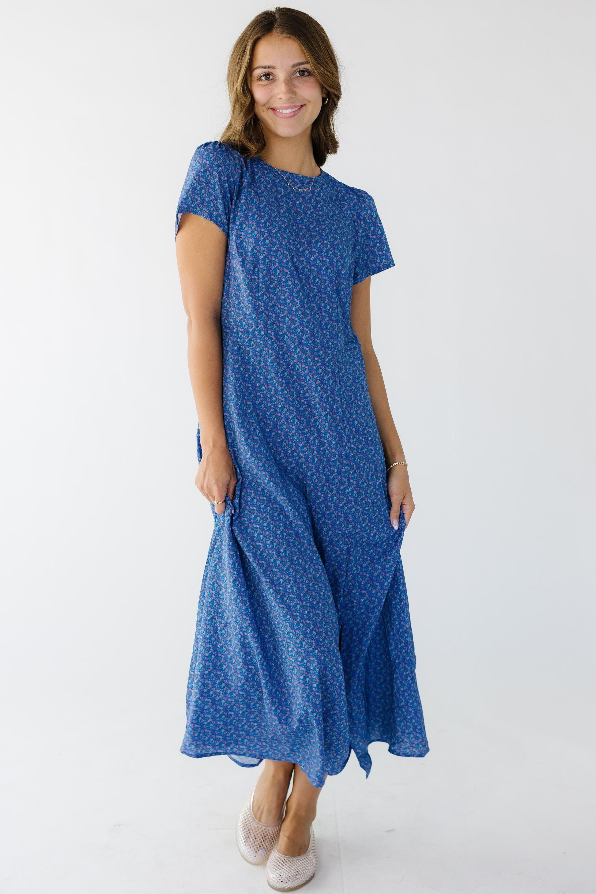 Woman wearing a modest blue floral midi dress with a round neckline, short sleeves and an off center front slit.
