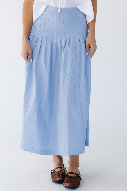 Young woman wearing a modest blue midi skirt with sewn down pleats all around the hip.