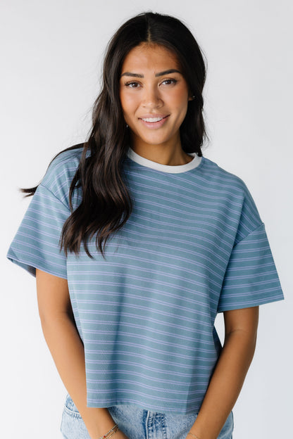 Woman wearing a boxy green tee with blue double stripes with short sleeves and a white crew neckline.