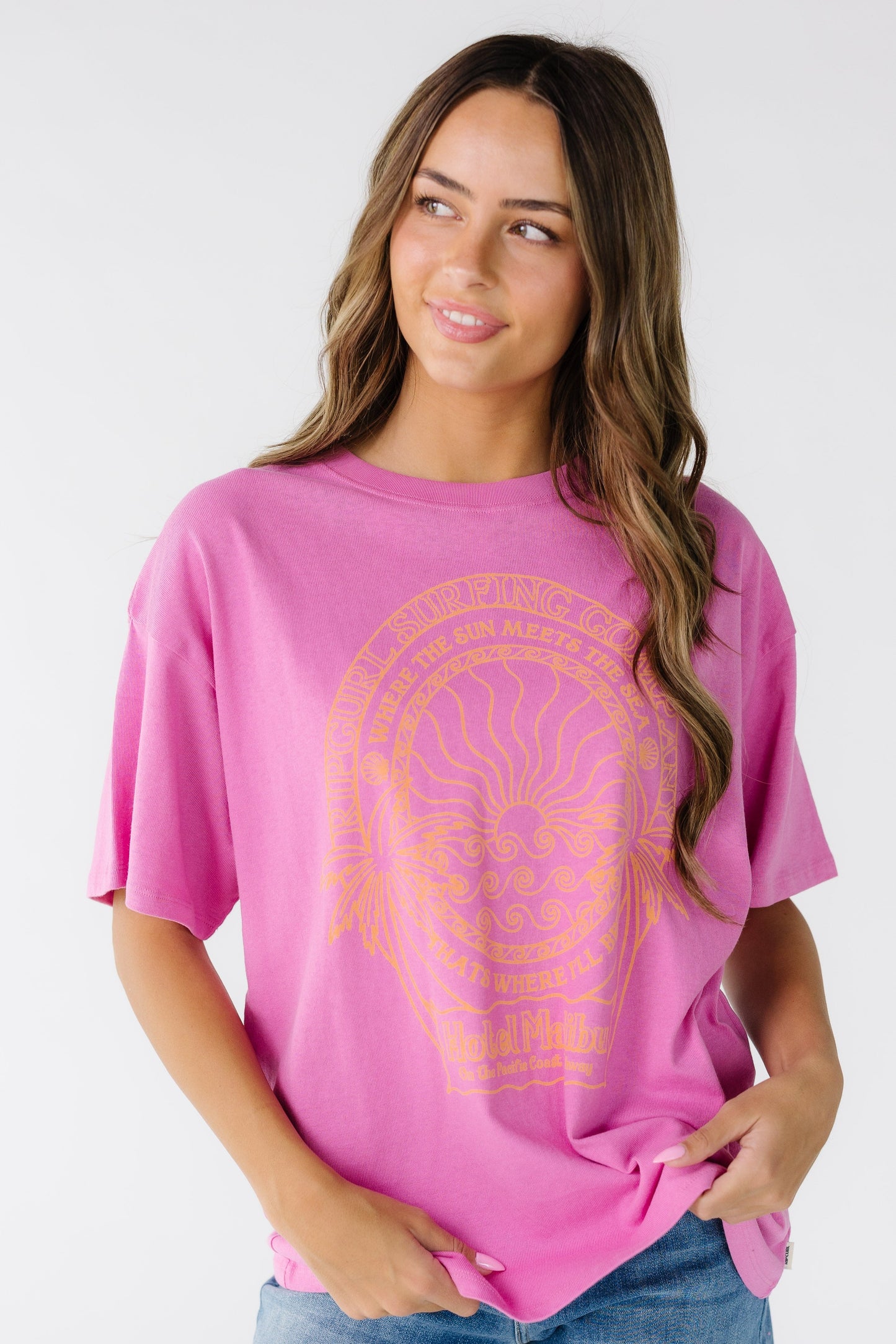 Young woman wearing a pink short sleeve graphic tee made by Rip Curl. 