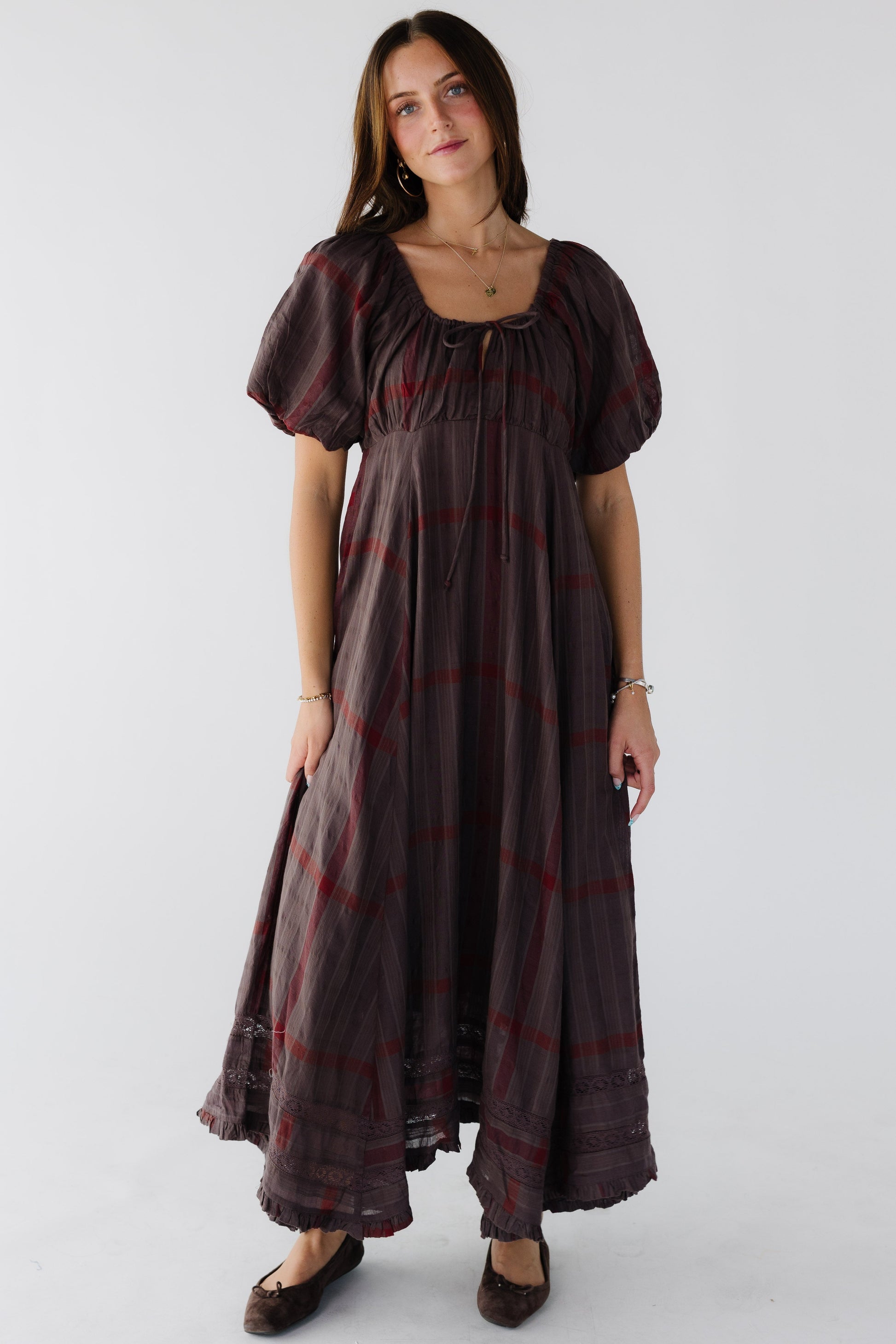 Woman wearing a loose fitting brown plaid midi-maxi dress wiht an empire waist and balloon sleeves and a drawstring scoop neckline.