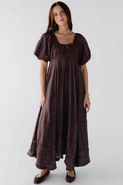 Woman wearing a loose fitting brown plaid midi-maxi dress wiht an empire waist and balloon sleeves and a drawstring scoop neckline.