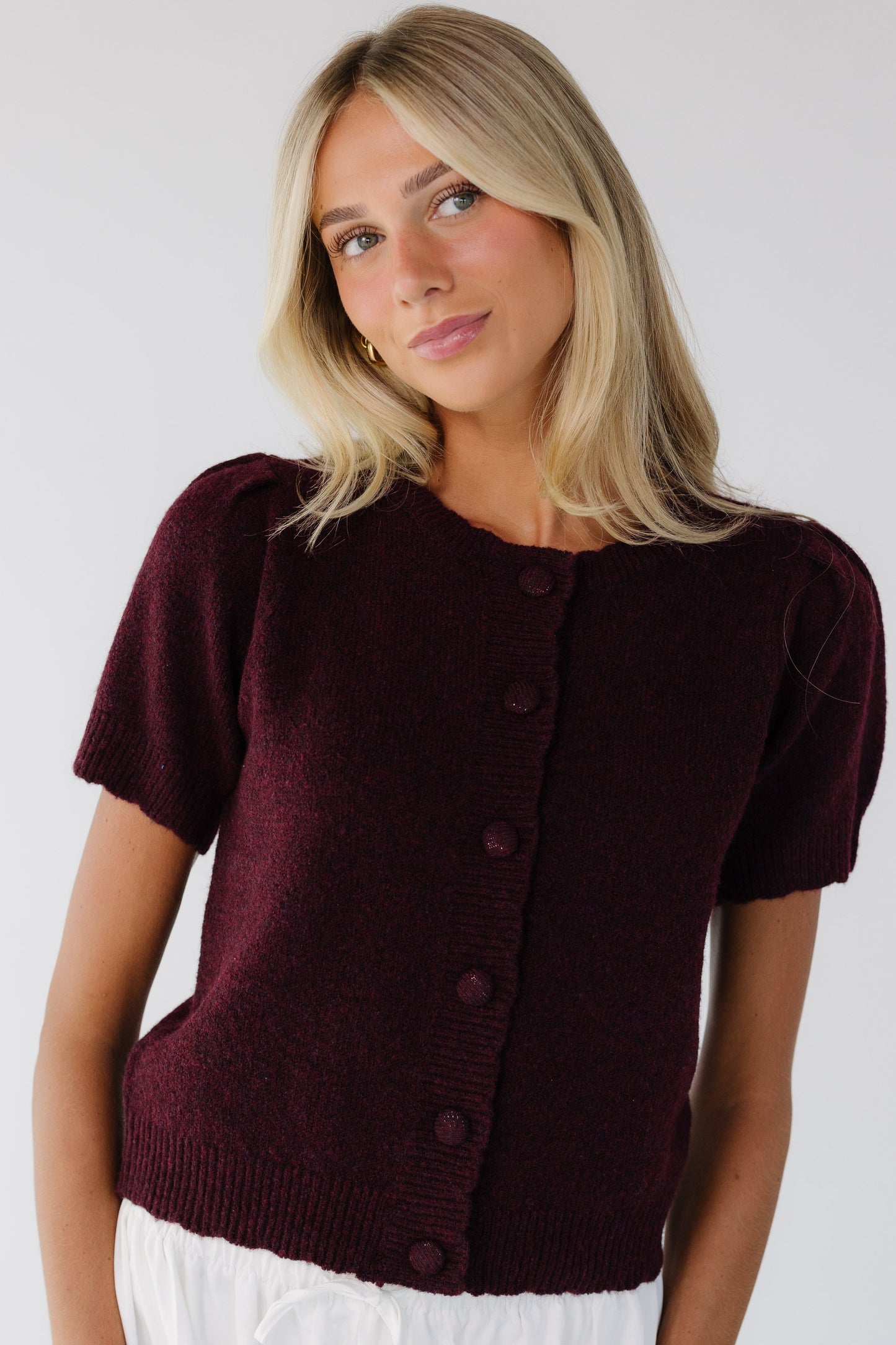 Young woman wearing a modest burgundy button down cardigan with scallop hems & collar with short sleeves.