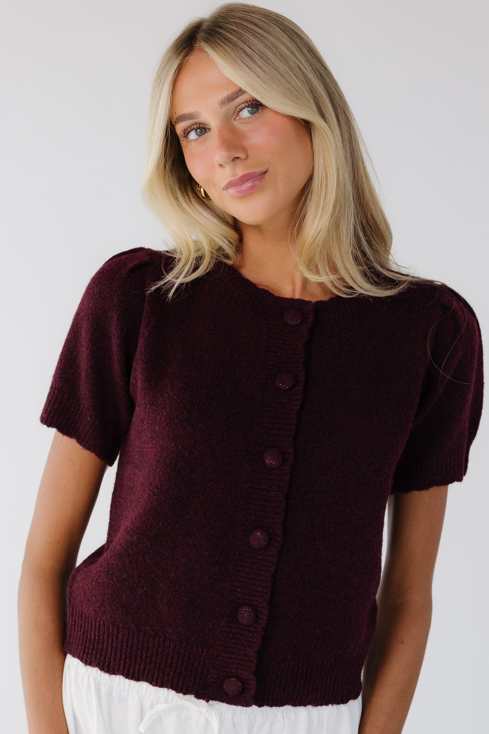 Young woman wearing a modest burgundy button down cardigan with scallop hems & collar with short sleeves.