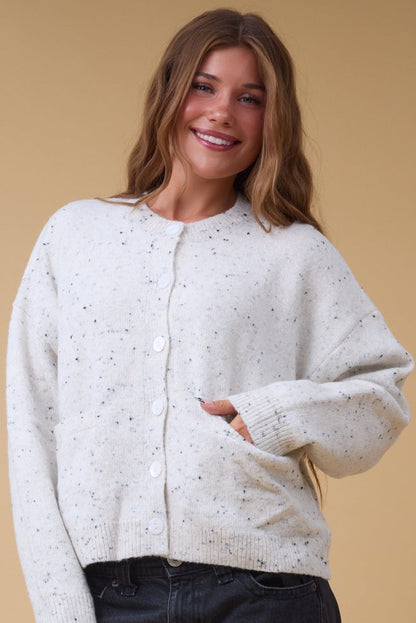 Young woman wearing a  modest cream flecked button down cardigan with front pockets, long sleeves and a crew neckline.