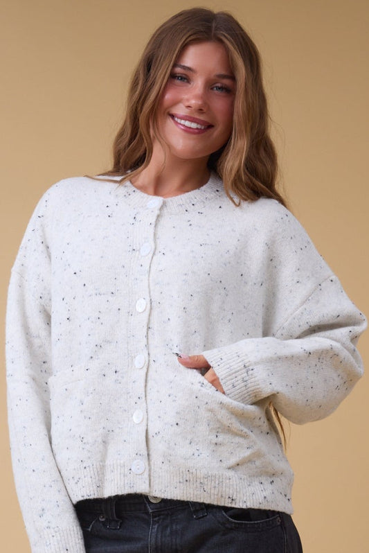 Young woman wearing a  modest cream flecked button down cardigan with front pockets, long sleeves and a crew neckline.