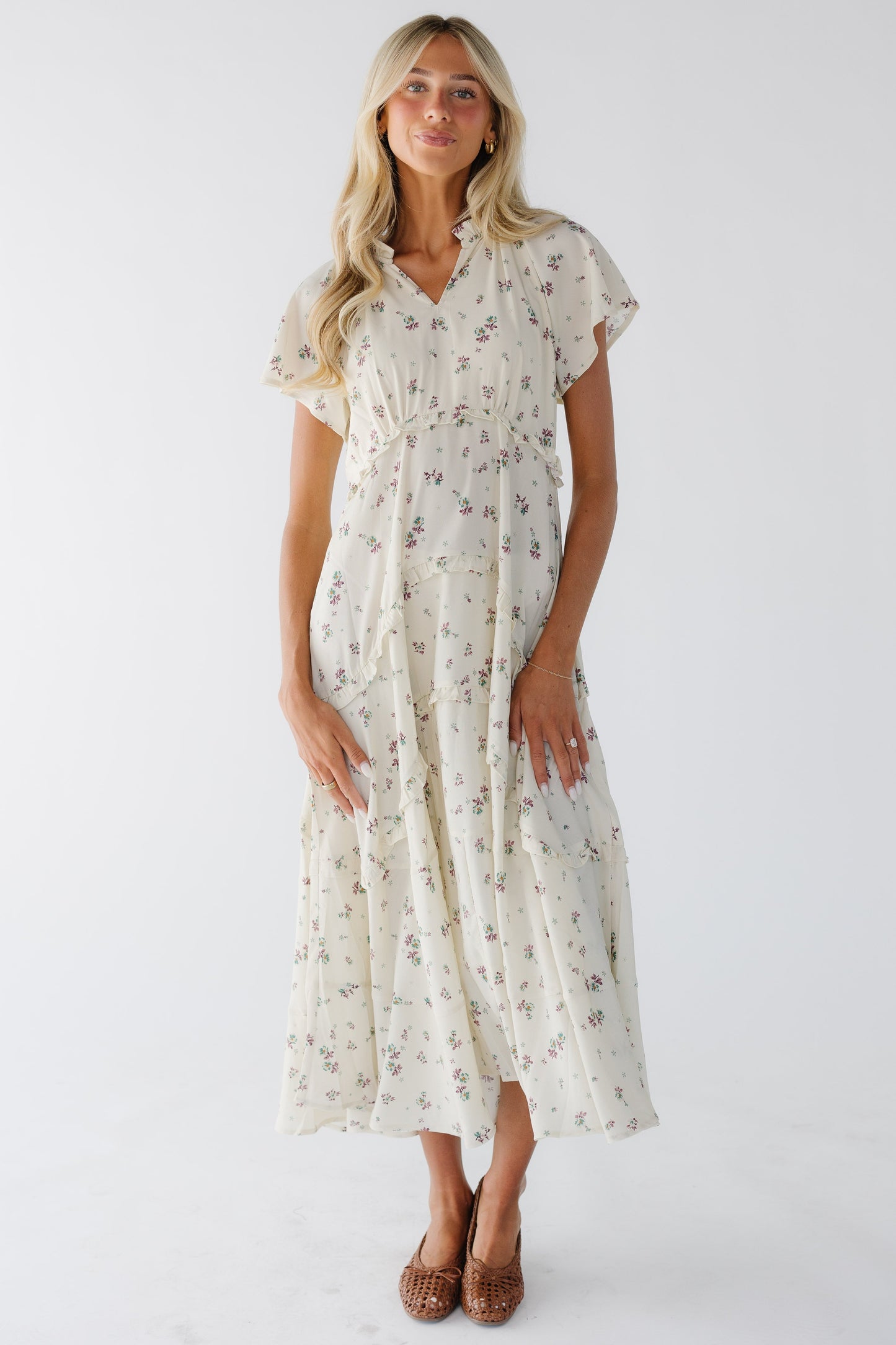 Woman wearing a loose fitting cream and lavender print midi-maxi dress witn an empire waist.