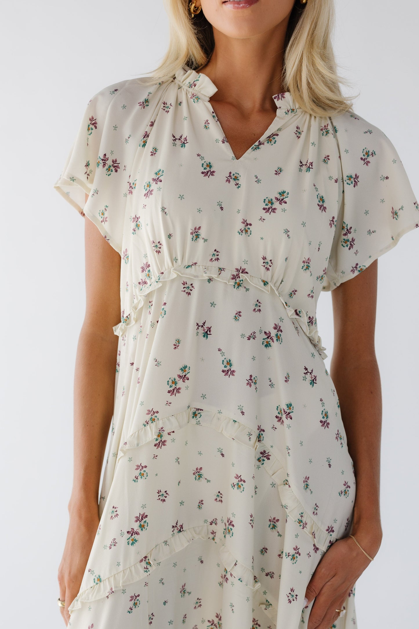 Young woman wearing a cream & lavender floral print midi dress with a curved empire waist, short sleeves and a V-neckline.