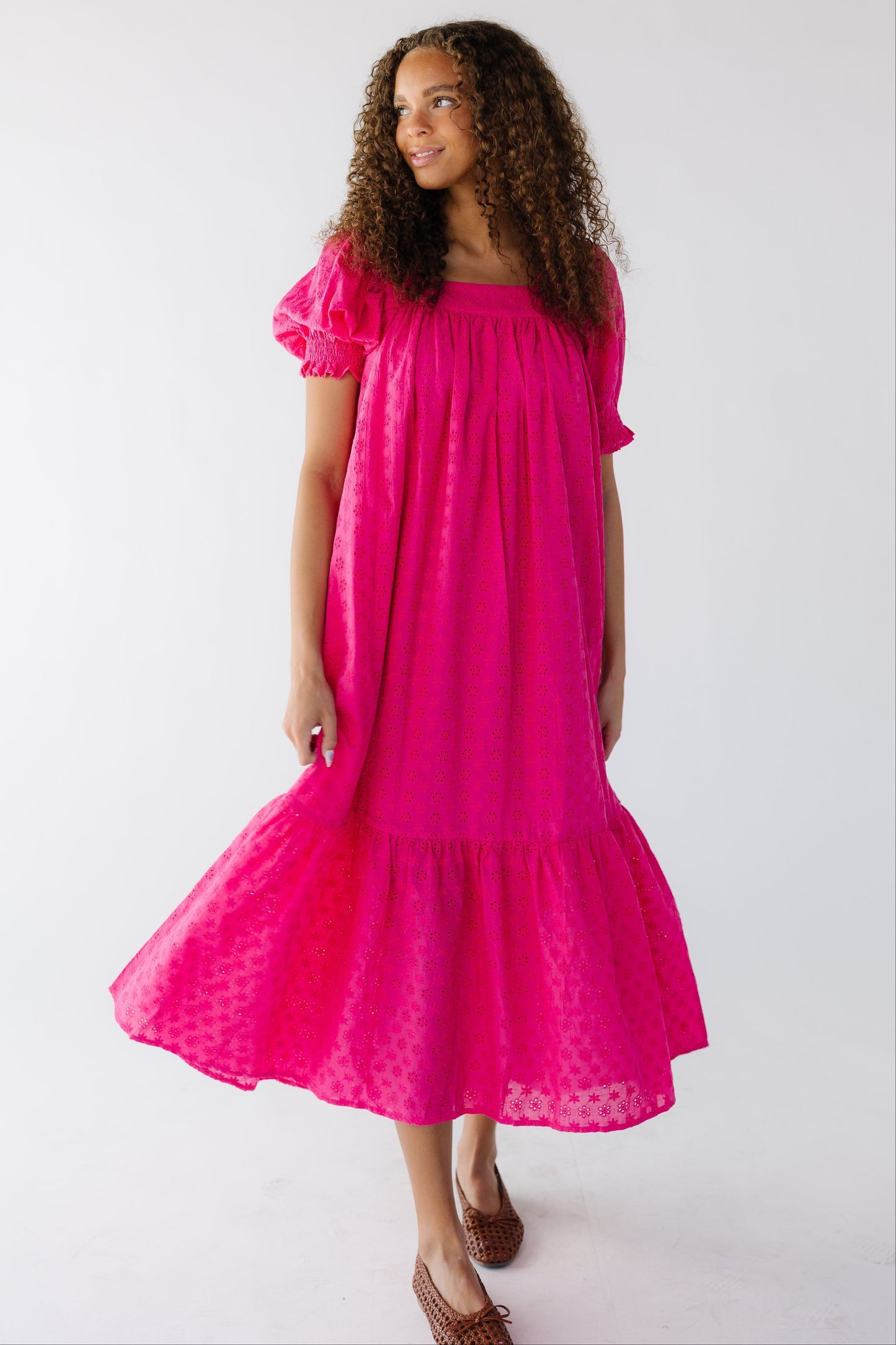 Teen girl wearing a loose fitting swing midi dress in bright pink eyelet  with a wide bottom ruffle, Square neckline and large puff sleeves with a smocked cuff.