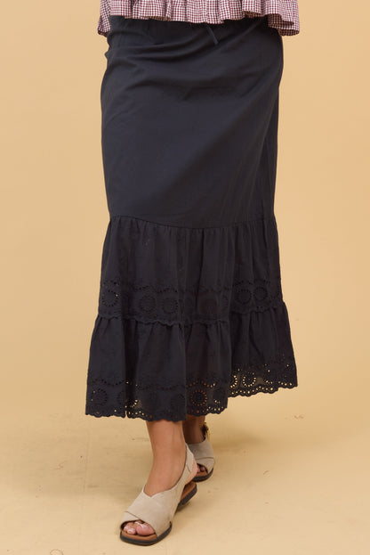 Woman wearing a black midi skirt with a wide eyelet bottom ruffle.