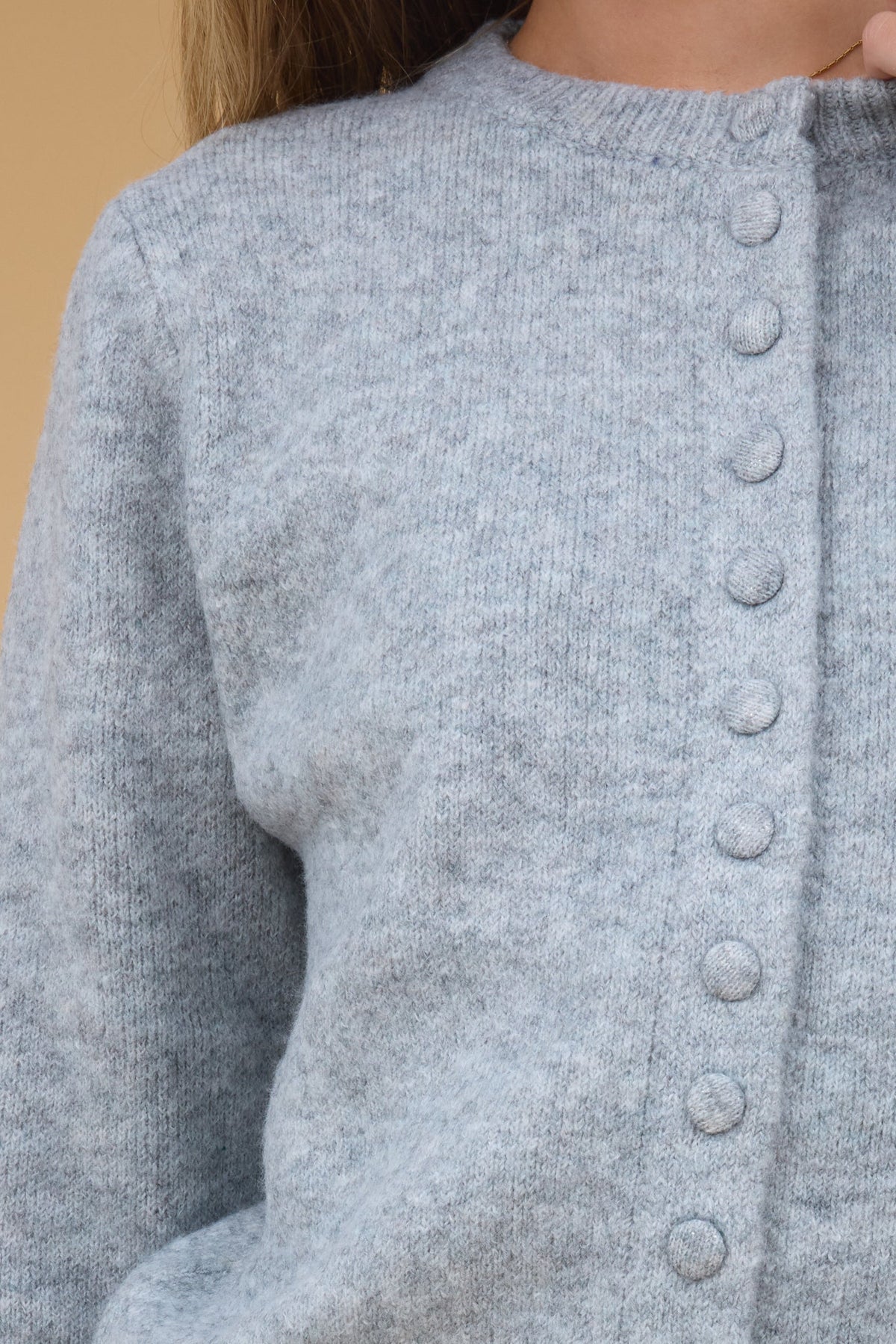 Close view of a young woman wearing grey cardigan with matching covered buttons.