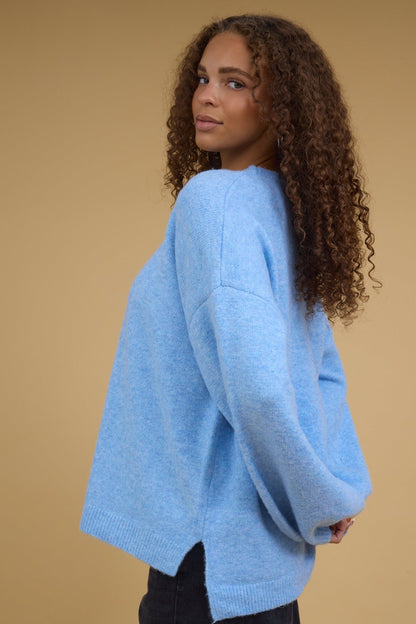 Young woman wearing a loose fitting pullover sweater with drop shoulders, long sleeves and a high-low hemline.