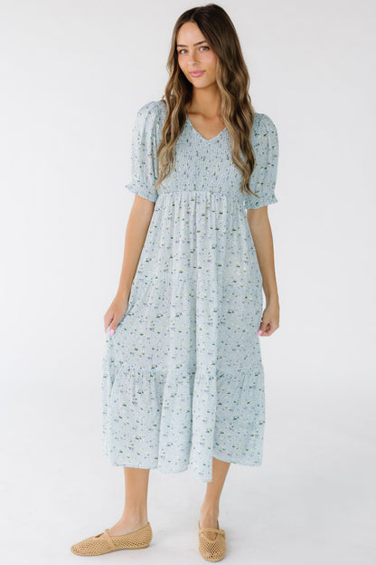 Woman wearing a light blue floral tiered midi dress with a V-Neckline and smocked front and back bodice.