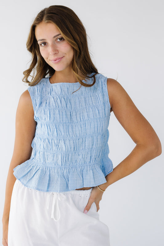 Young woman wearing a modest, sleeveless, light blue smocked blouse with a bottom ruffle and a round neckline.