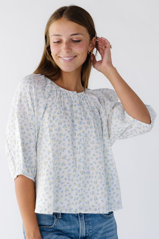 Young woman wearing a modest loose fitting, button down swing top in white with blue floral print and elbow length sleeves.
