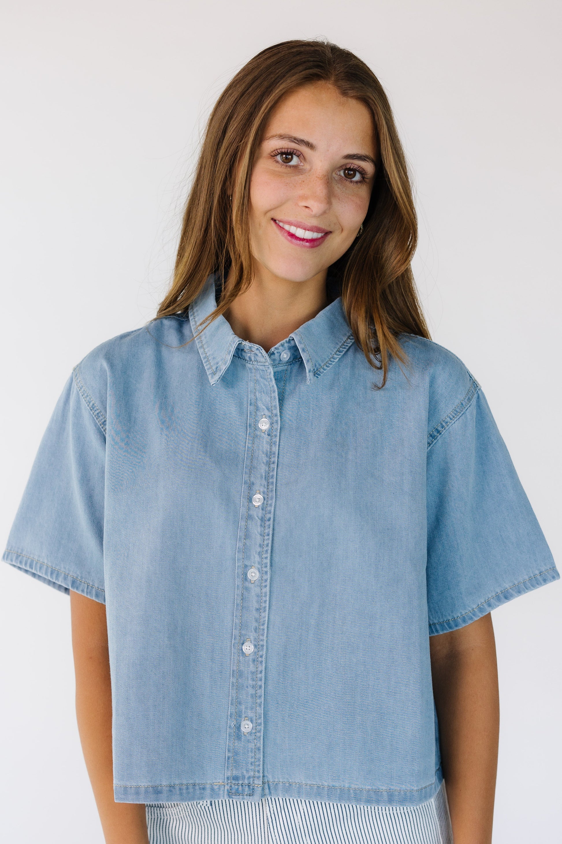 Woman wearing a modest button down top with a pointed collar, short sleeves and a  straight cut hem.