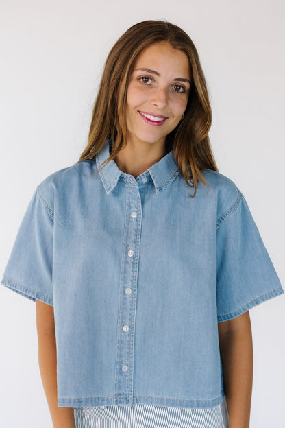 Woman wearing a modest button down top with a pointed collar, short sleeves and a  straight cut hem.