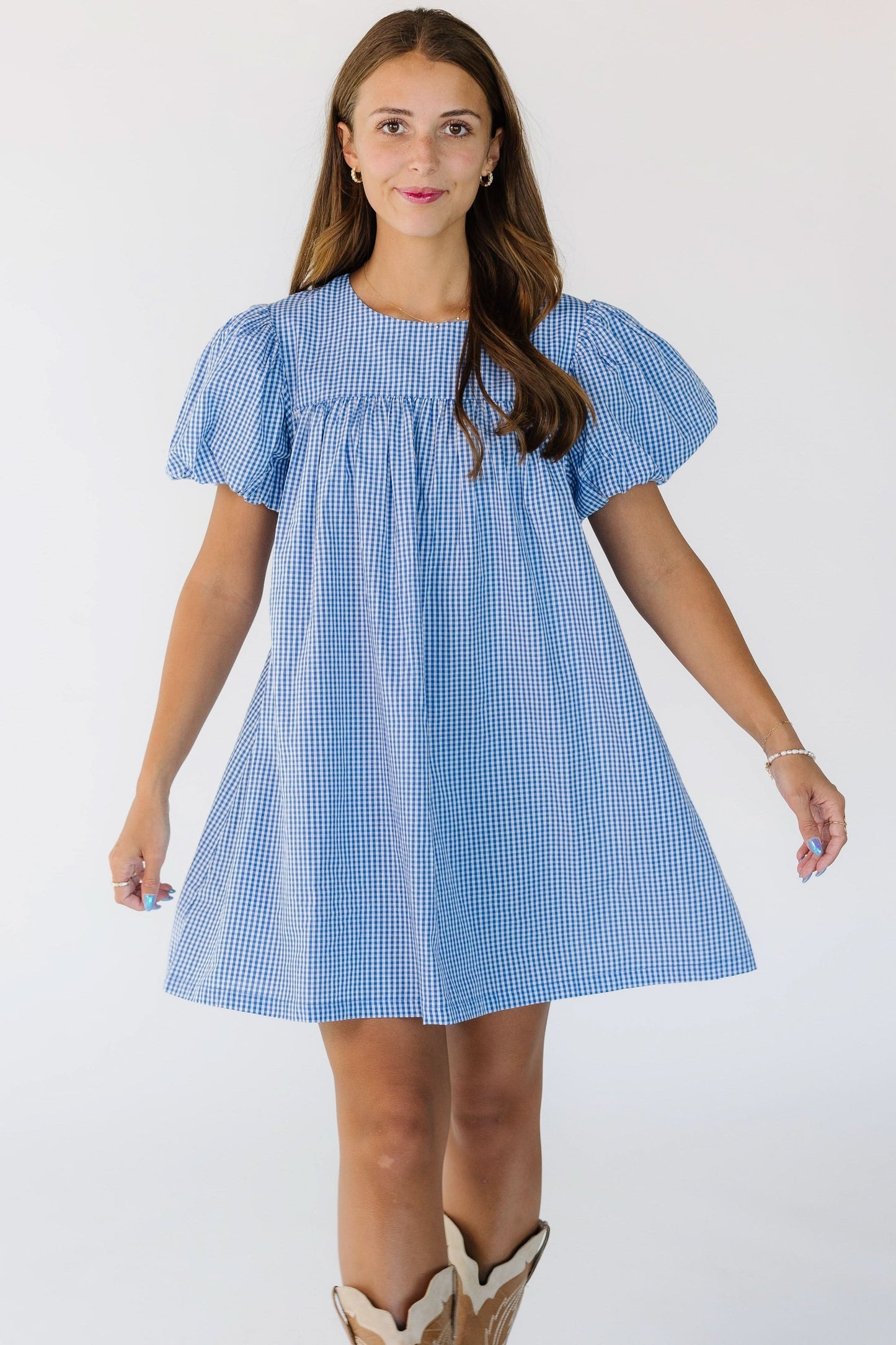 Woman wearing a short mini dress in a blue and white gingham  with large puff sleeves.