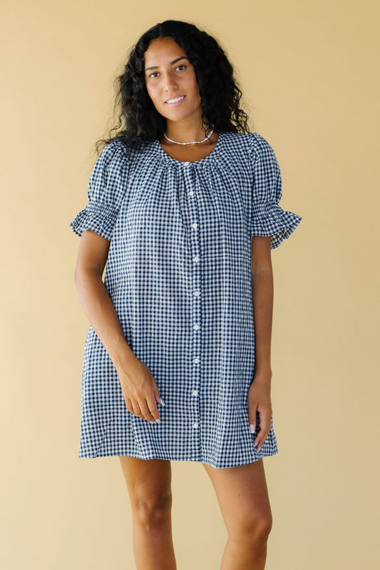 Young woman wearing a modest navy & white gingham loose fitting, button down dress with a scoop neckline and puff sleeves.