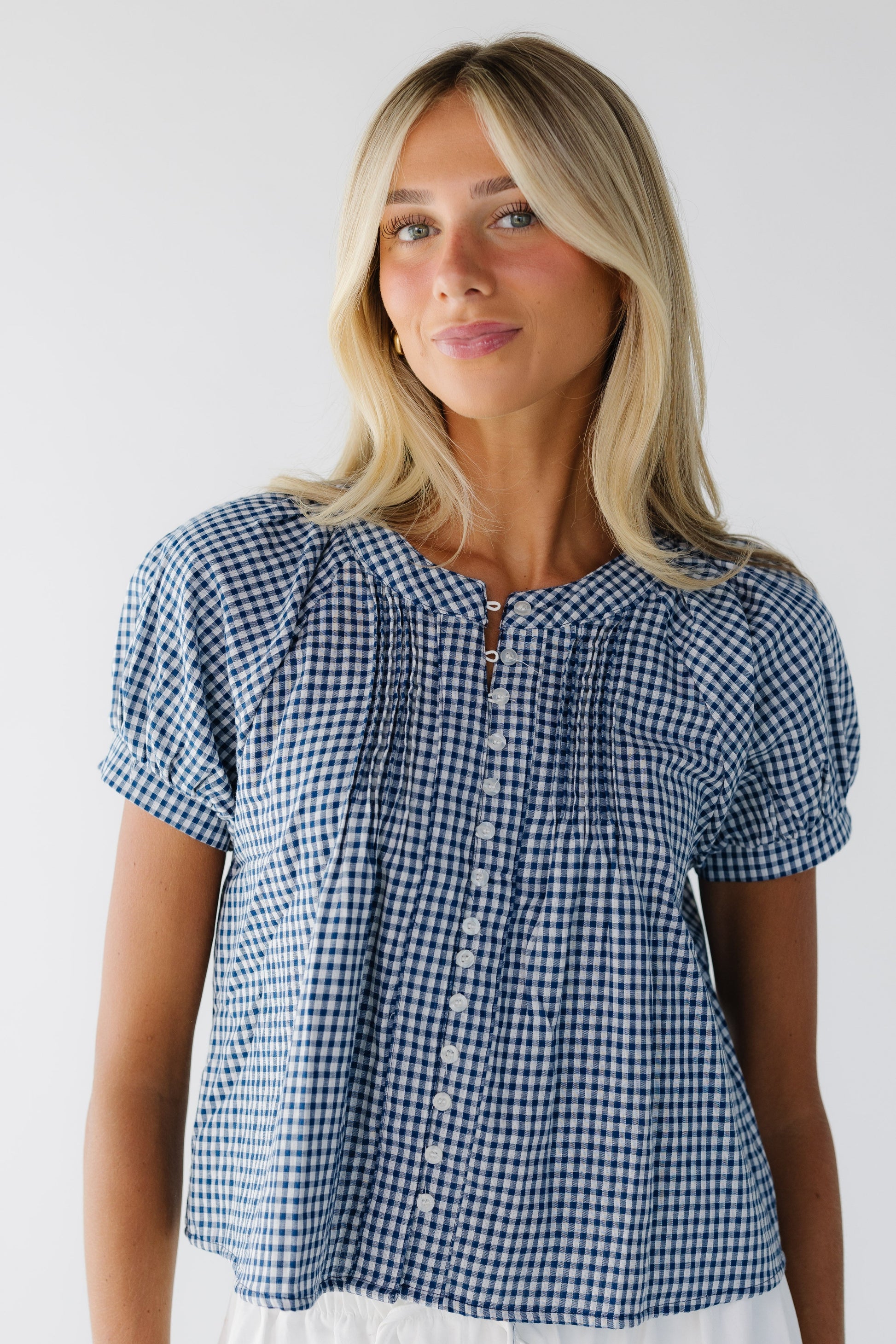 Young woman wearing a modest navy & white gingham button down blousewith shrot puff sleeves and front pleats.