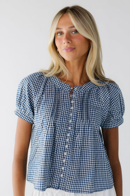 Young woman wearing a modest navy & white gingham button down blousewith shrot puff sleeves and front pleats.
