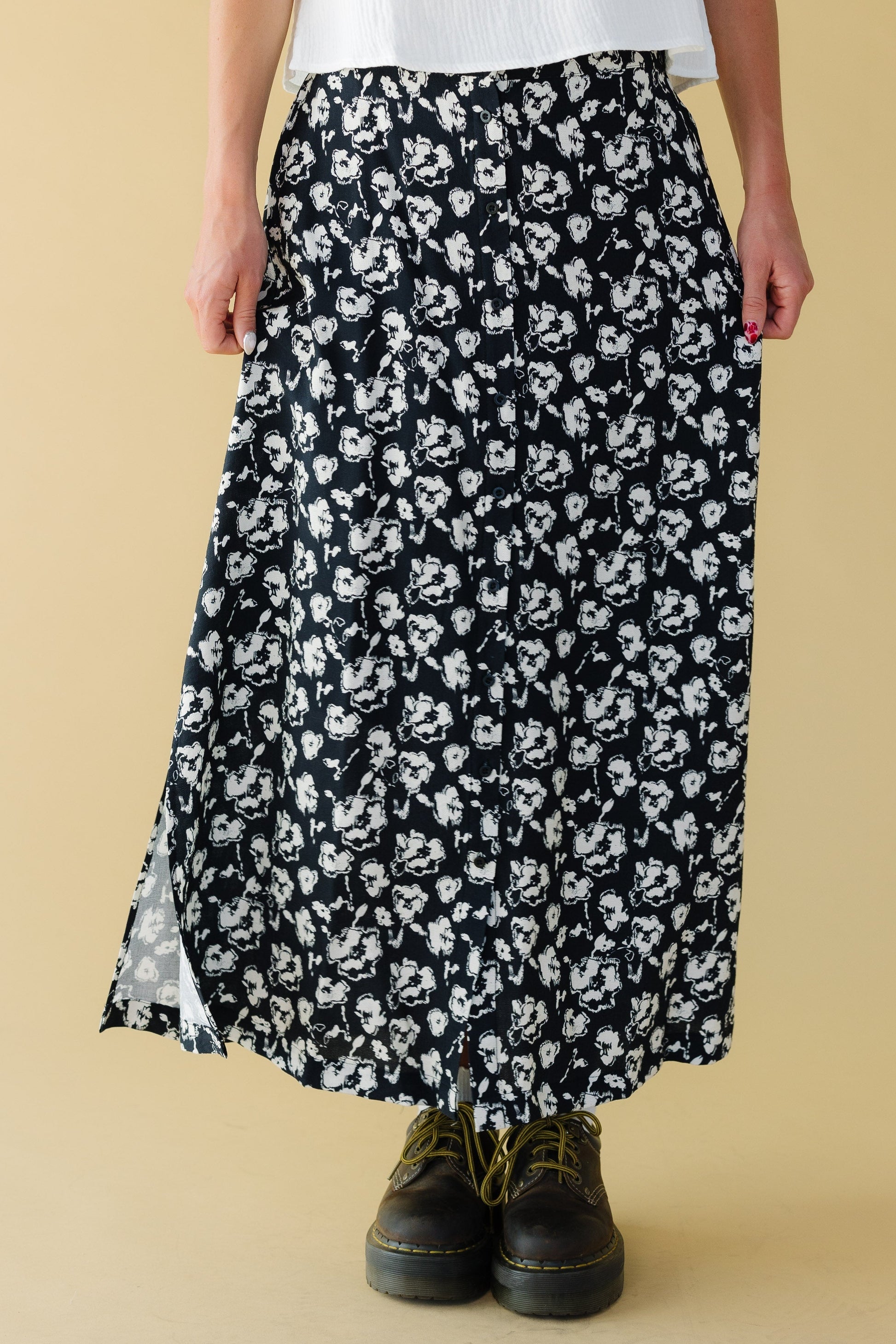 Woman wearing a full loose fitting midi skith that buttons down the front with short side slits.