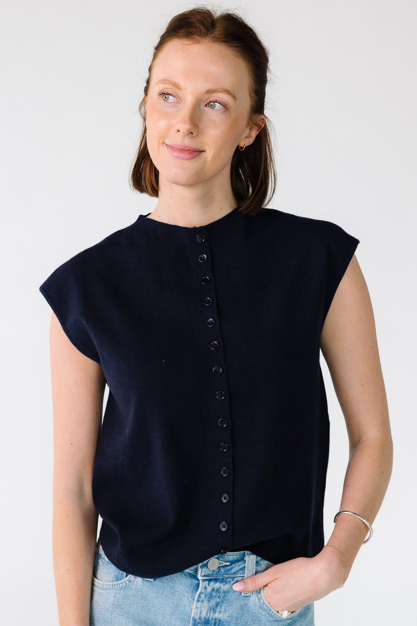 Woman wearing a loose fitting button down sweater vest with a high round collar in navy.