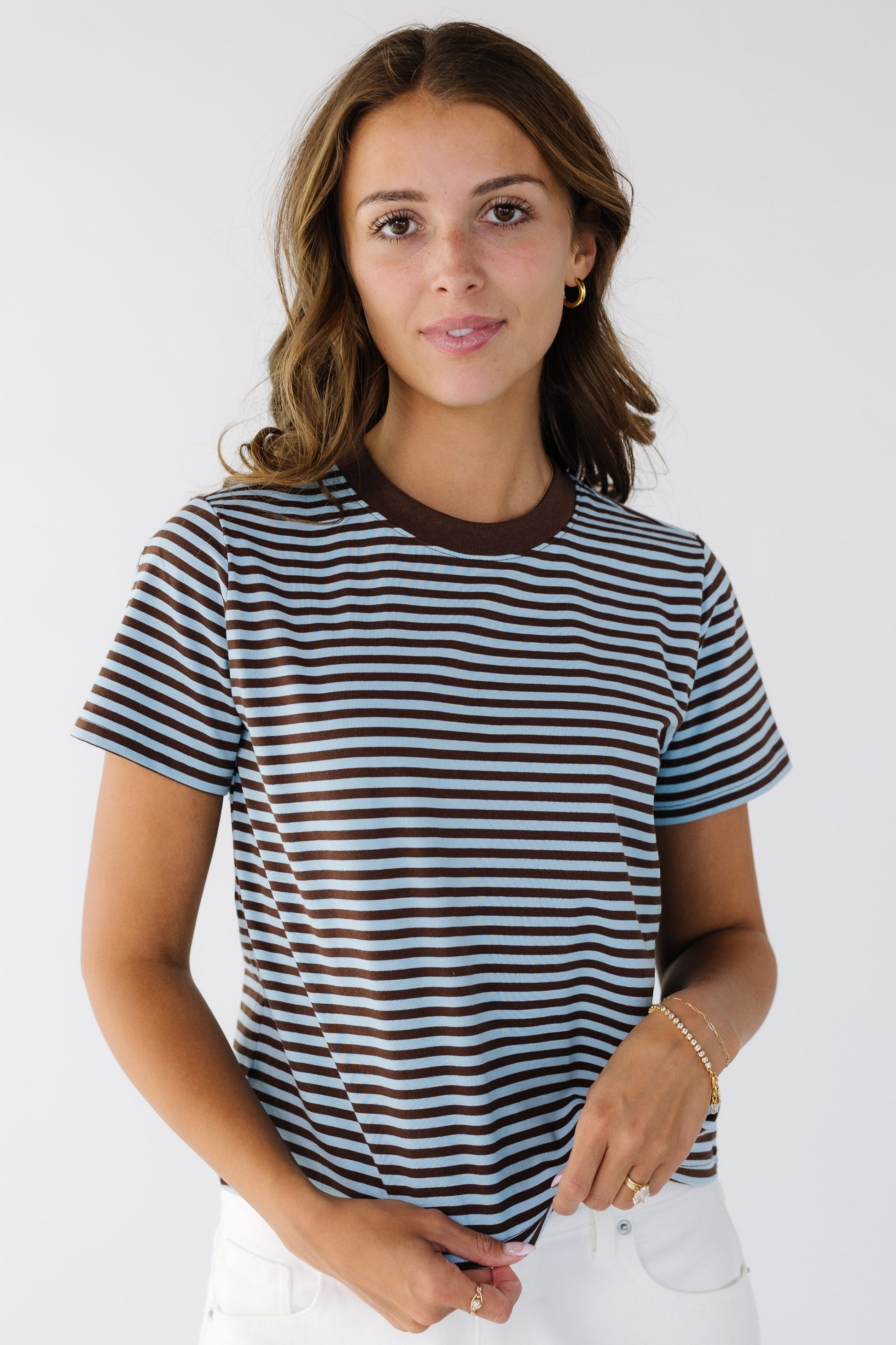 A young woman wearing a brown and blue stripe t-shirt with a crew neckline and short sleeves.