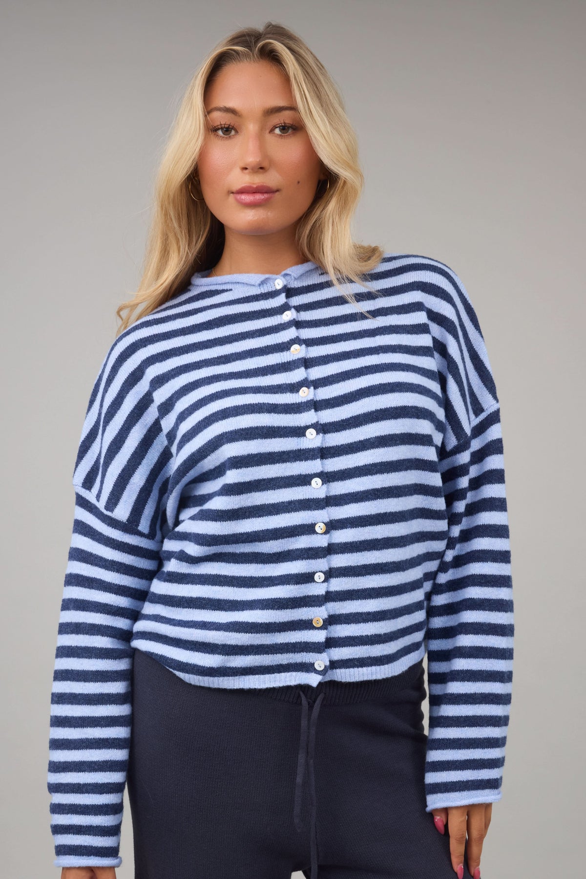 Woman wearing a slightly loose fitting button down cardigan with drop shoulders and long sleeves.