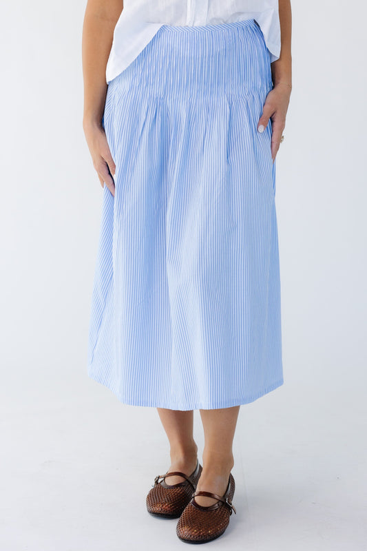 Young woman wearing a modest  blue and white striped midi skirt with sewn down pleats around the hip.