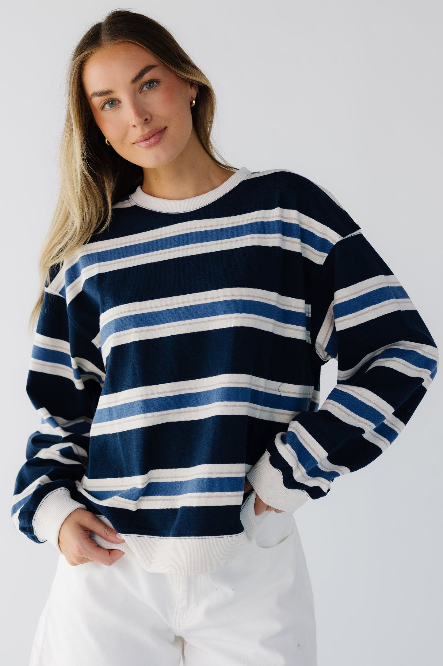 Woman wearing a loose fitting navy, blue & white stripe top with ribbed cuffs and a round crew neckline.